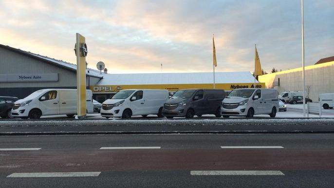 Flere varevogne parkeret foran en bygning med gule flag og sne på jorden.