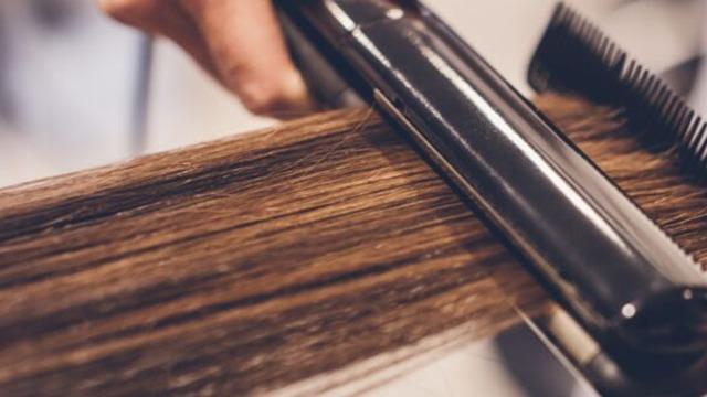 En hånd bruger en glattejern til at style brunt hår i en frisørsalon.