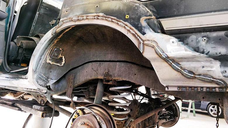 Billede af en bils undervogn med synlige affjedringskomponenter og rustne metaldele under reparation.