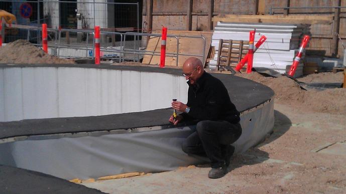 En mand sidder på kanten af en cirkulær konstruktion, mens han arbejder med materialer på en byggeplads.