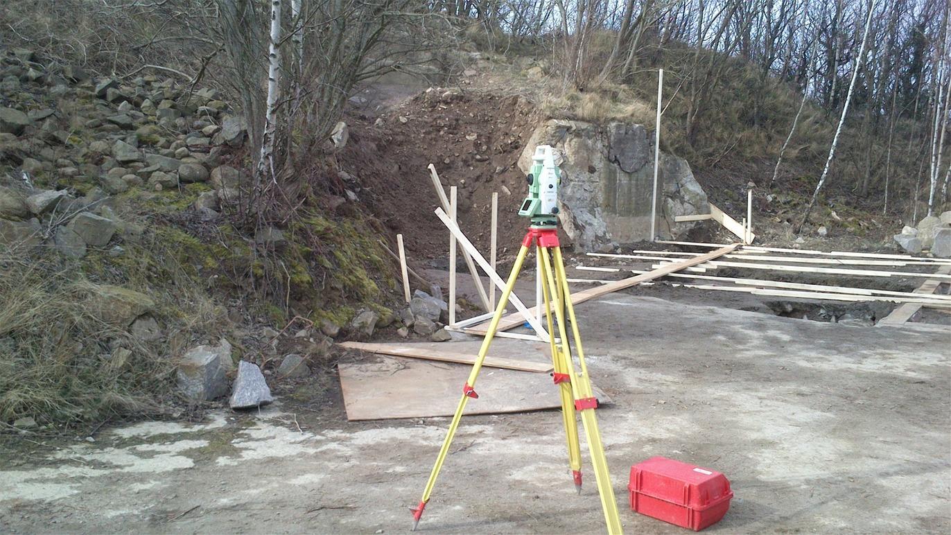 Et byggeplads med en totalstation, trærammer og en skrænt i baggrunden.