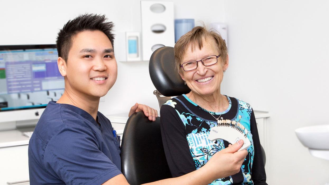 En tandlæge viser en ældre kvinde et farvekort til tandfarve i en tandklinik.