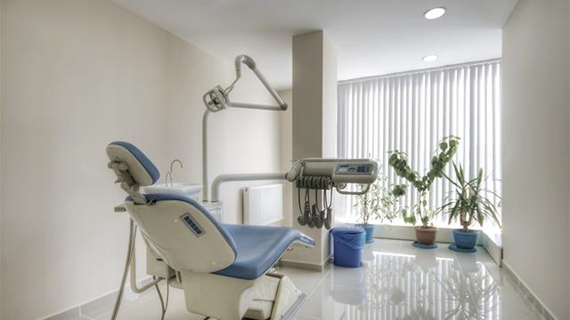 Moderne tandlægeklinik med en tandlægestol, planter og store vinduer, der giver naturligt lys.