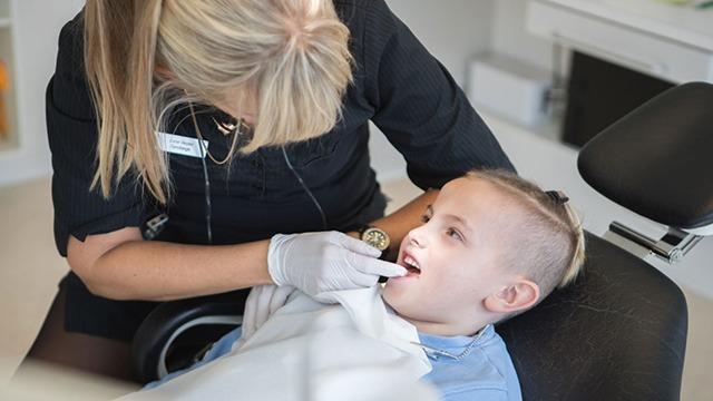 En tandlæge undersøger en ung drengs tænder i en moderne tandklinik.