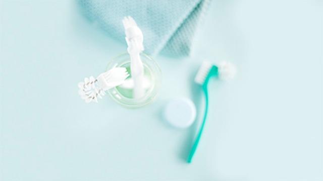 Toothbrush and toothpaste in a glass on a light blue background with a towel nearby.
