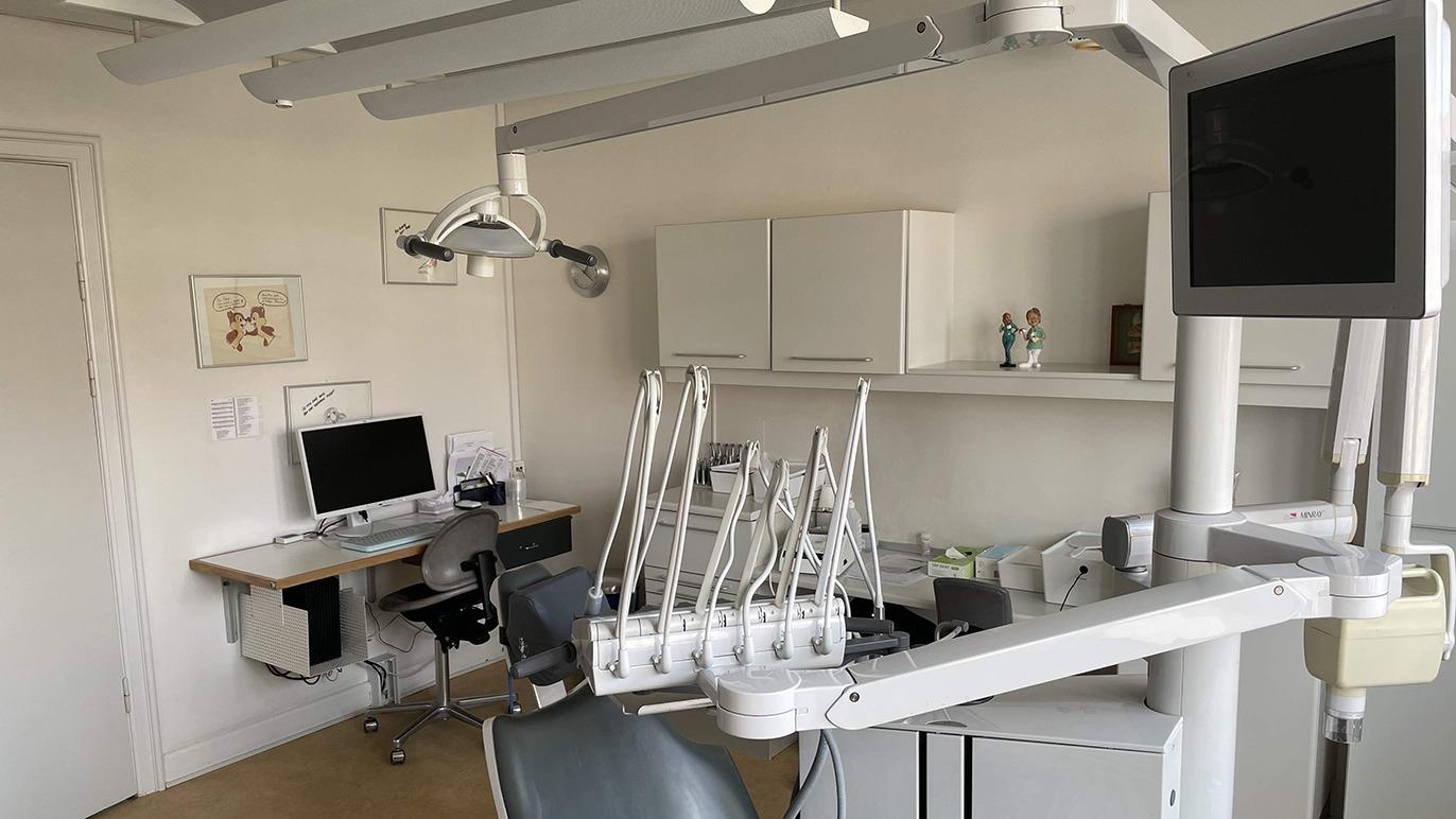 Moderne tandlægeklinik med udstyr, computer og behandlingsstol i et lyst rum.
