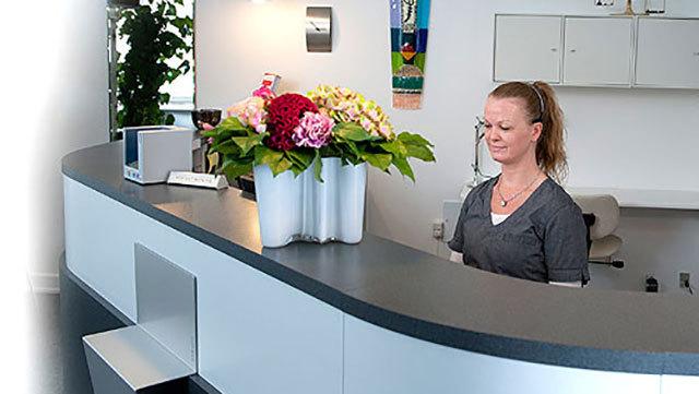 En receptionist står ved en moderne skranke med en blomsterbuket i en vase.