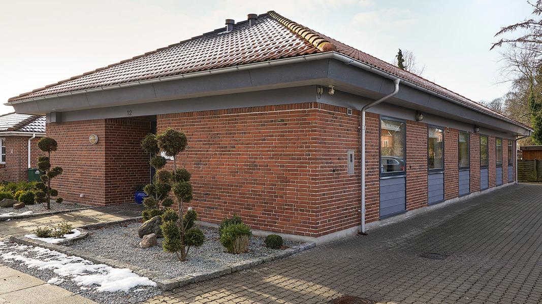 En moderne murstensvilla med fladt tag og store vinduer, omgivet af velplejede buske og en grusbelagt indkørsel.