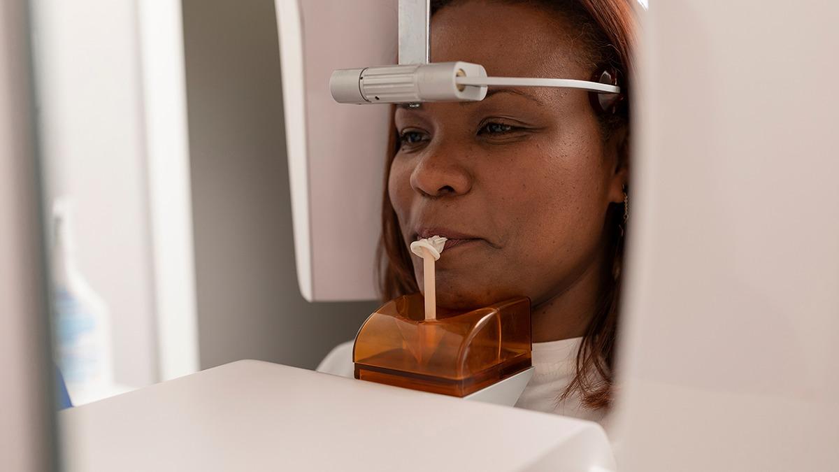 Kvinde får tandrøntgen i tandlægeklinik med ansigtet placeret i en røntgenmaskine.