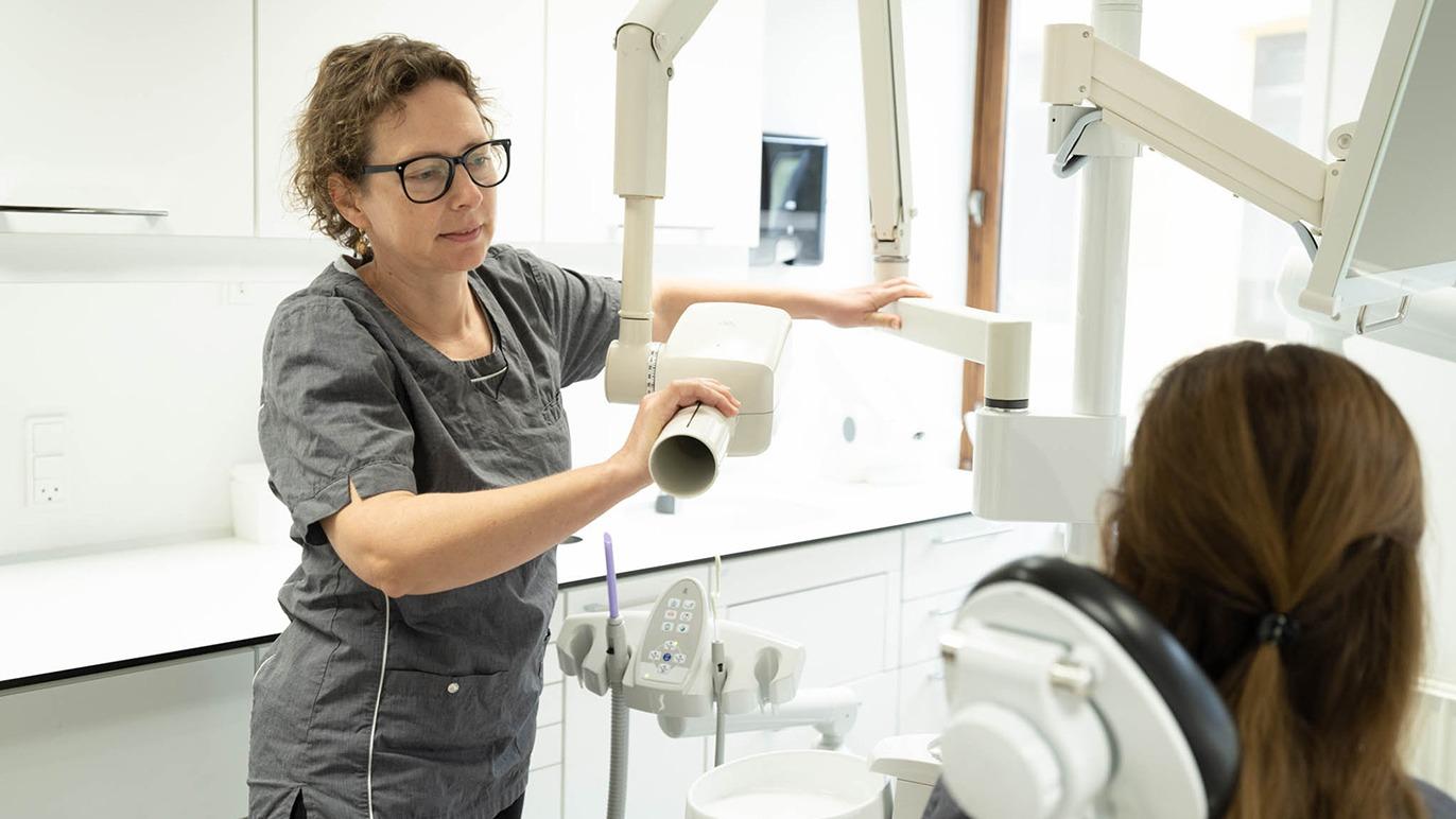 En tandlæge i grå uniform forbereder en røntgenmaskine til en patient i en moderne tandklinik.