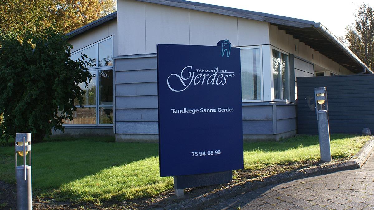 Skilt med teksten "Gerdes" foran en moderne bygning med store vinduer og græsplæne.