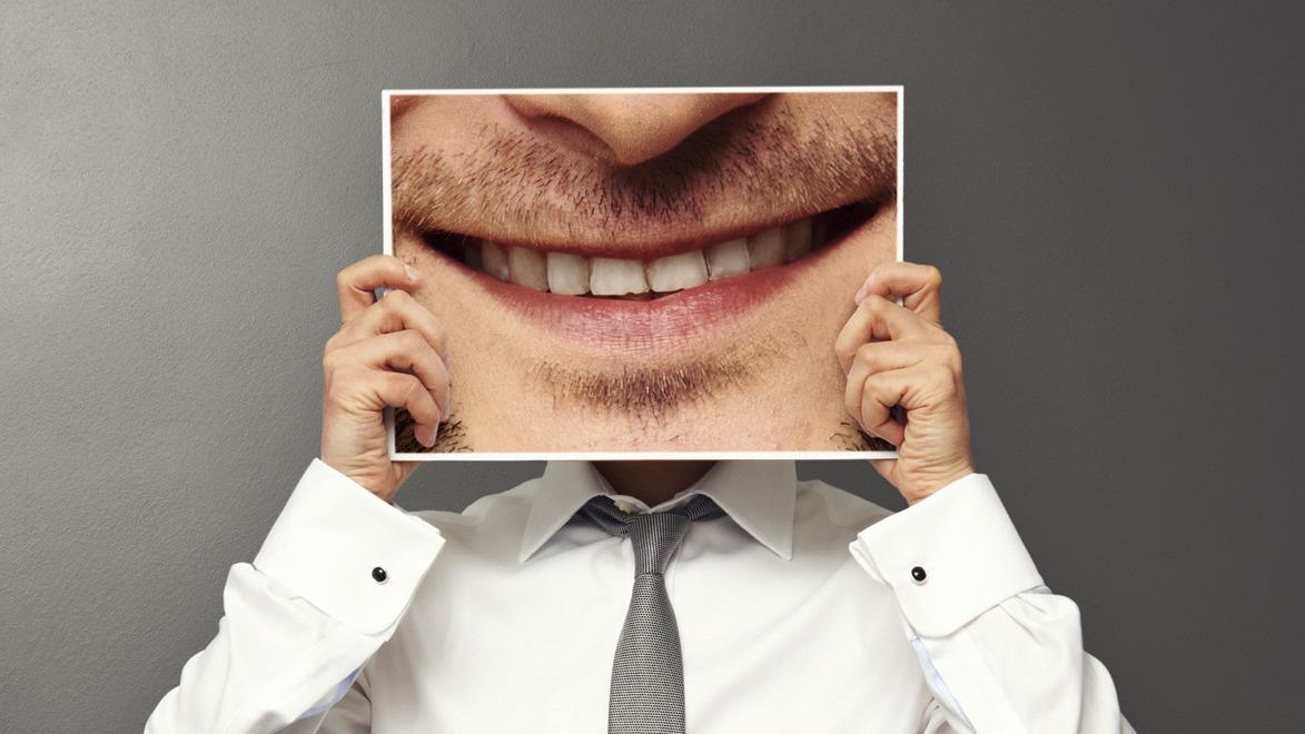 En person i skjorte holder et billede af et smil foran sit ansigt.