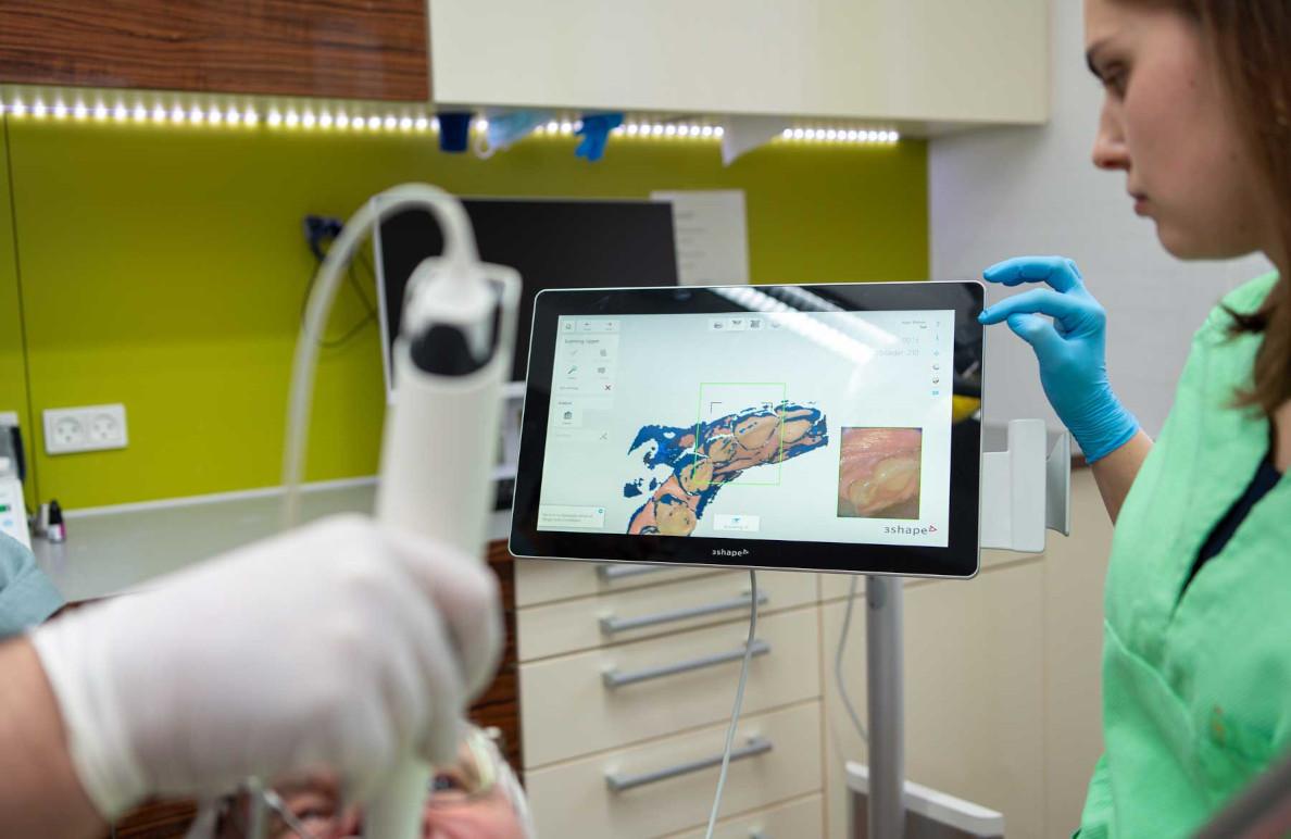 En tandlægeassistent bruger en digital skærm til at vise en tandbehandling i en moderne tandklinik.