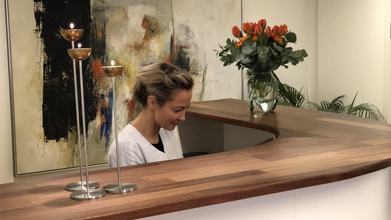 En kvinde sidder ved en reception med en blomsterbuket og stearinlys i baggrunden.