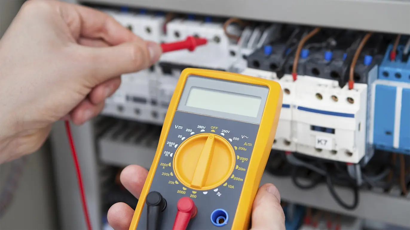 En person bruger et multimeter til at måle elektrisk spænding i en elektrisk tavle.