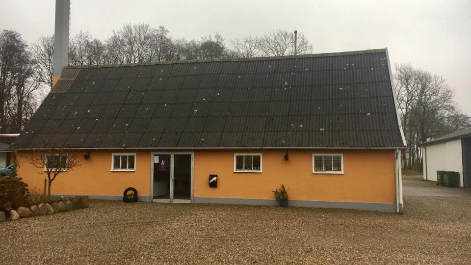 En orange hus med tag af teglsten, beliggende i et grusområde med træer i baggrunden.
