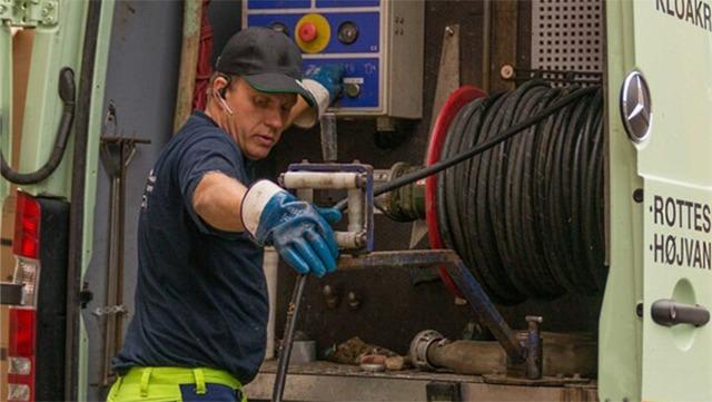 En mand i arbejdstøj arbejder med en slange fra en servicevogn til rensning af kloakker.