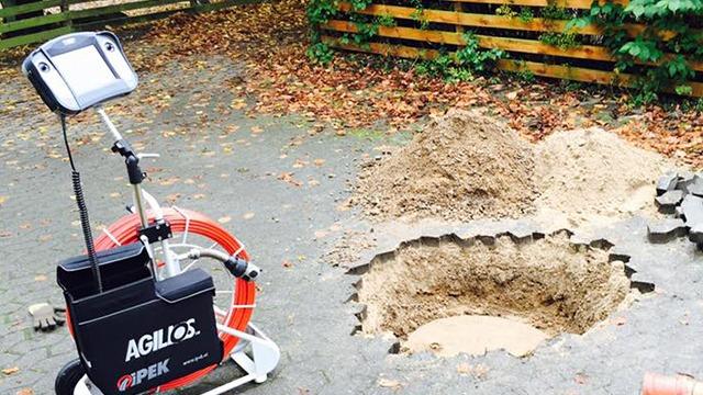 En AGILOS maskine står ved siden af et stort hul i jorden, omgivet af sand og grus.