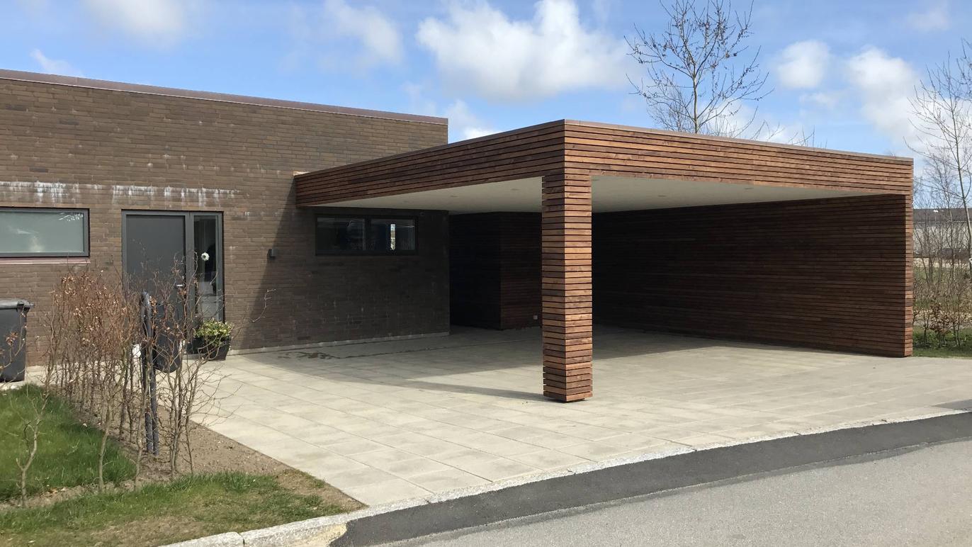 Moderne hus med en carport i træ og flisebelagt indkørsel under en blå himmel.