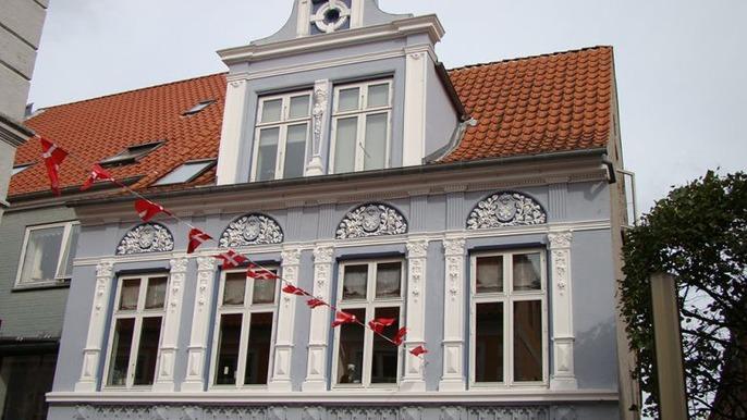 Et smukt hus med detaljeret facade og røde flag, beliggende i en by med historisk arkitektur.