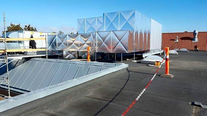 Tagkonstruktion med metalplader og ventilationsanlæg under installation på en bygning.