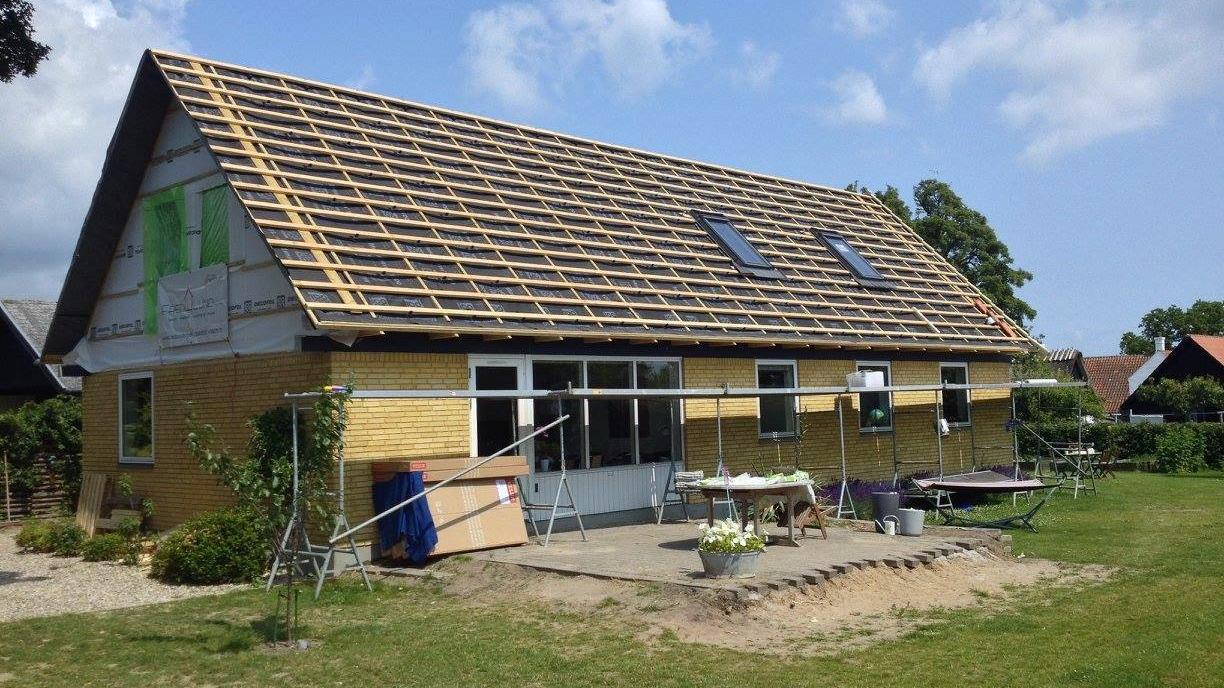 Nybygget hus med træbeklædning og tagarbejde, omgivet af græsplæne og haveudstyr.