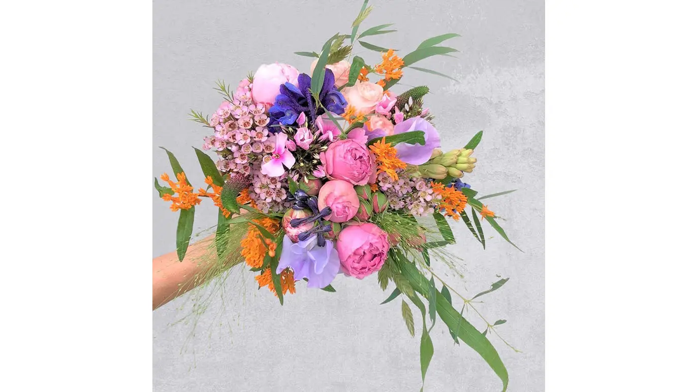 En farverig buket med lyserøde, lilla og orange blomster samt grønne blade.