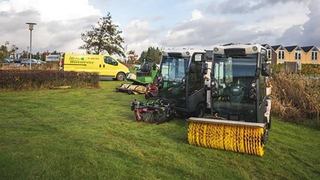 To store og moderne fejemaskiner parkeret på græsset ved siden af en gul servicevogn.