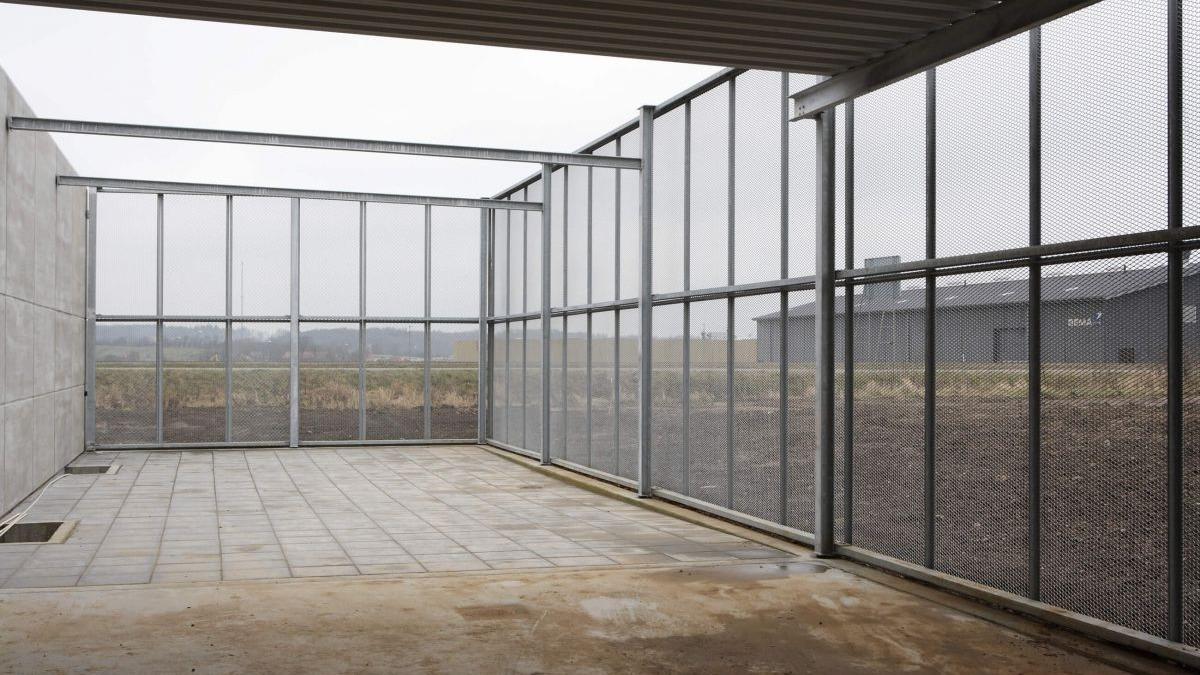 Tom indendørs område med metalgitter og betonvægge, der giver udsigt til det grå landskab udenfor.