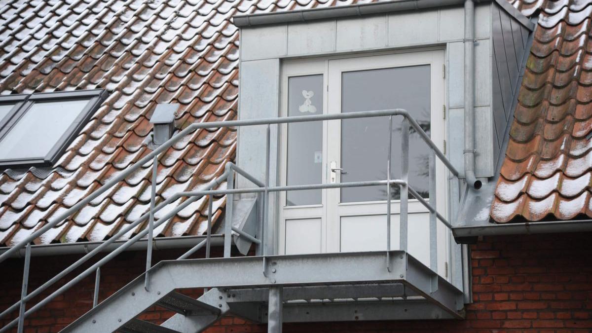 En udvendig trappe fører op til en dør på taget af en bygning med tagsten.