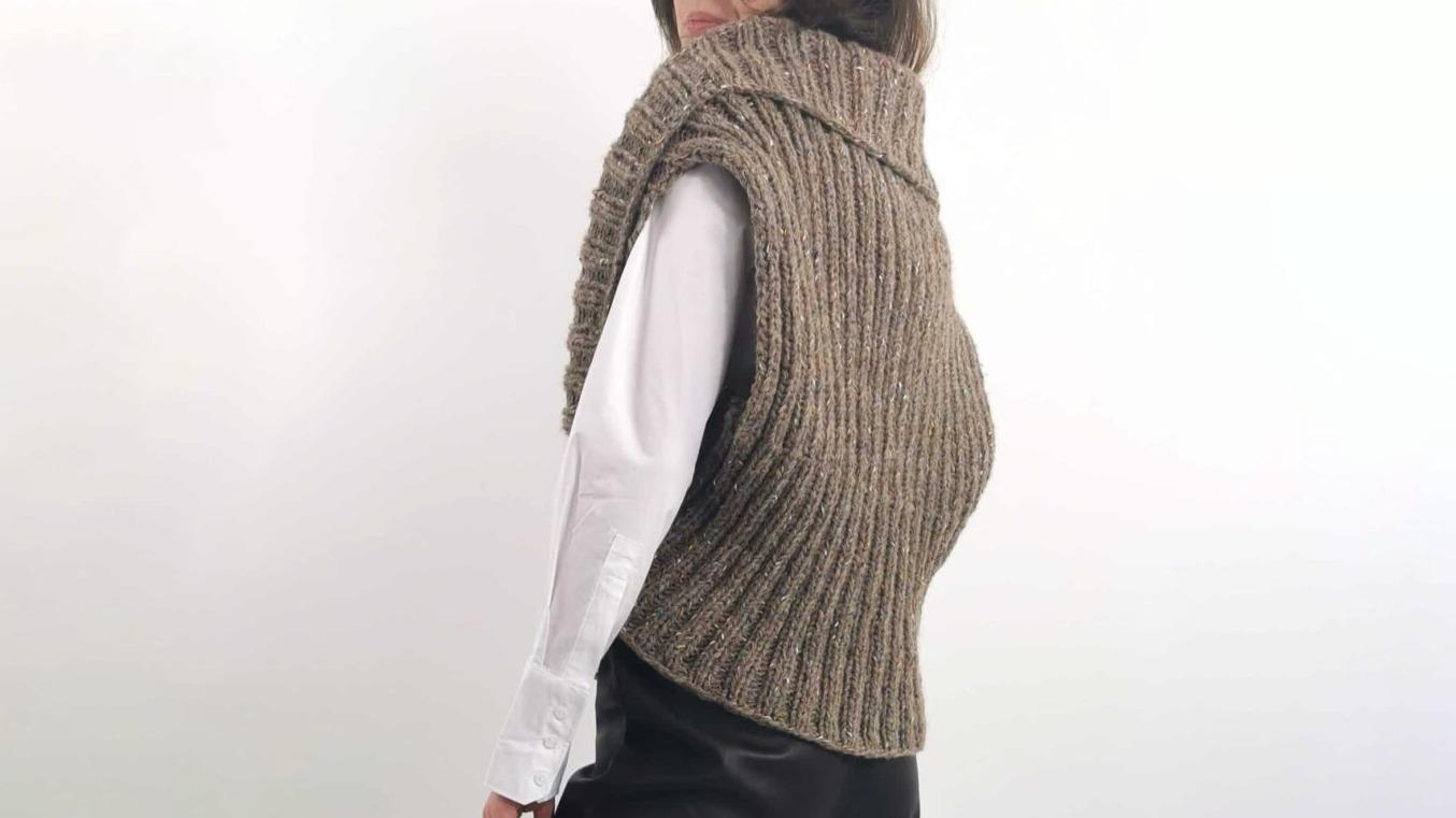 En person iført en strikket vest med høj krave, set fra siden, mod en lys baggrund.