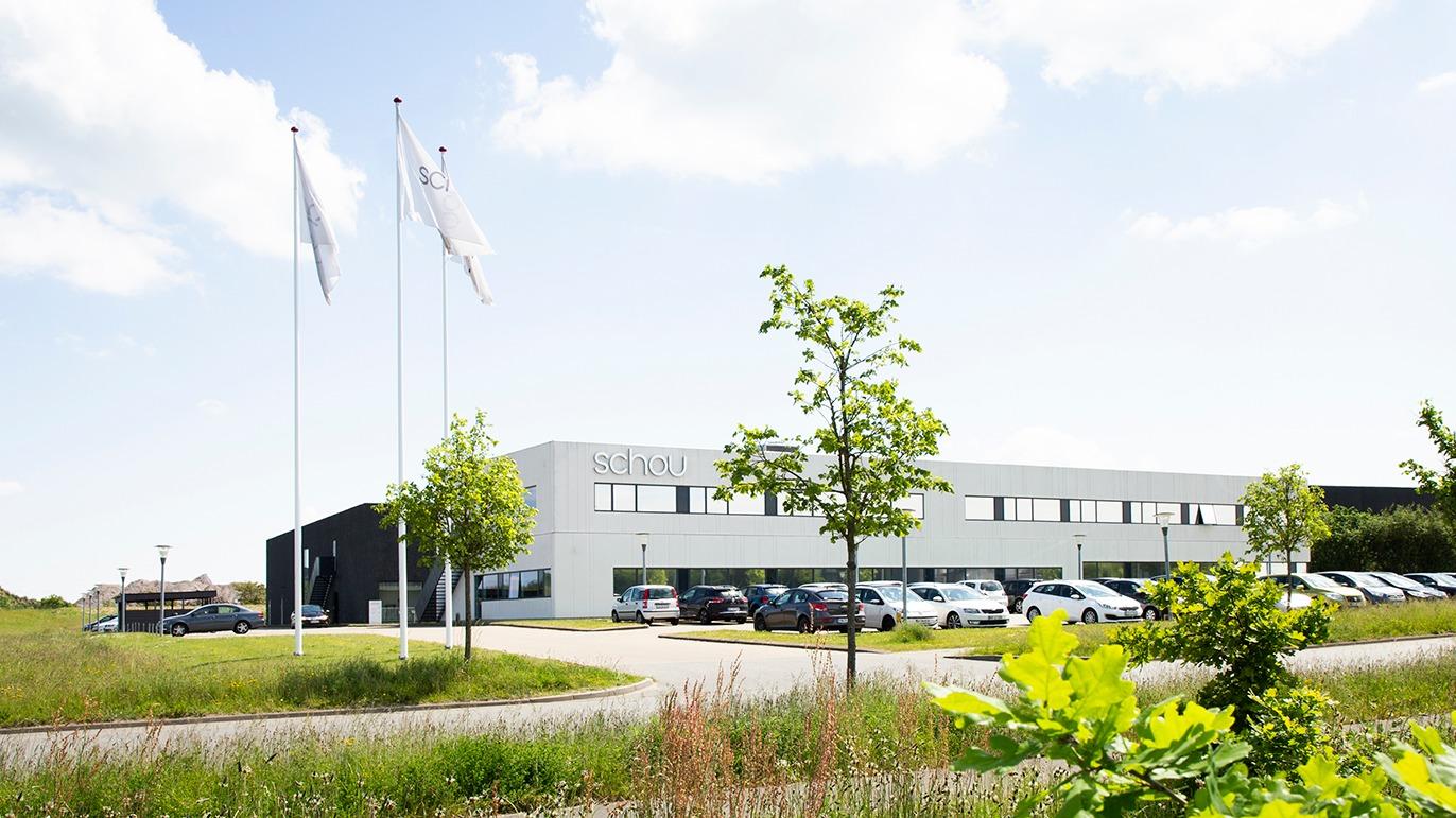Moderne kontorbygning med flagstænger og parkerede biler under en klar himmel.