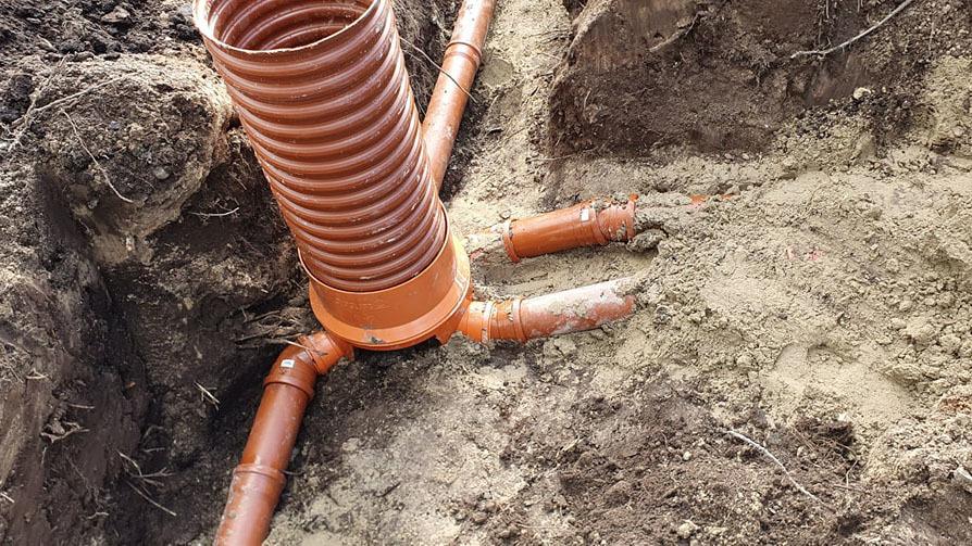 Rørinstallation i jorden med en orange brønd og tilsluttede rør i sandet.