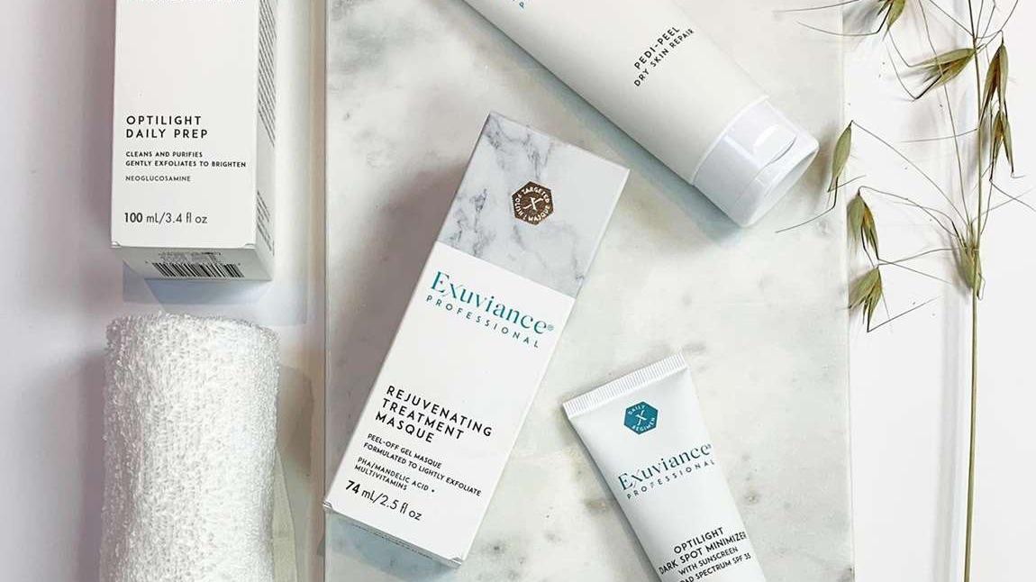 Billede af hudplejeprodukter på en marmoroverflade, herunder ansigtsskrubbe, serum og ansigtsmaske.