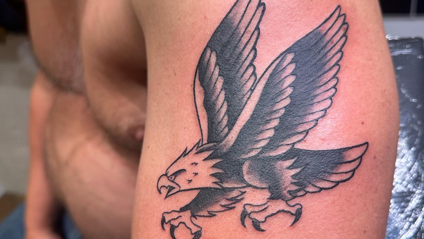 En tatovering af en stor ørn med udstrakte vinger på en mands overarm.