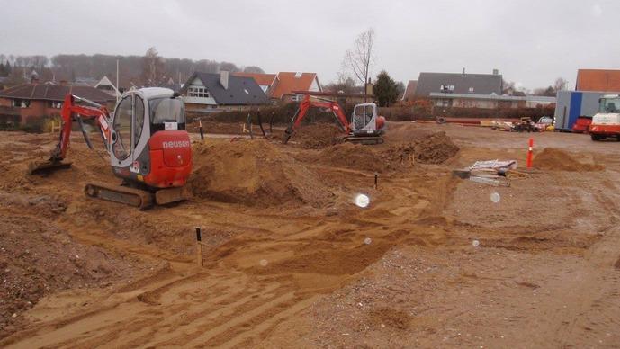 Byggeplads med gravemaskiner og jord, der er gravet op til fundamentarbejde i et boligområde.