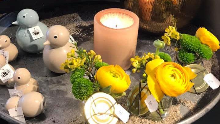 Dekorativt fad med farverige blomster, stearinlys og små fuglefigurer i pastelnuancer.