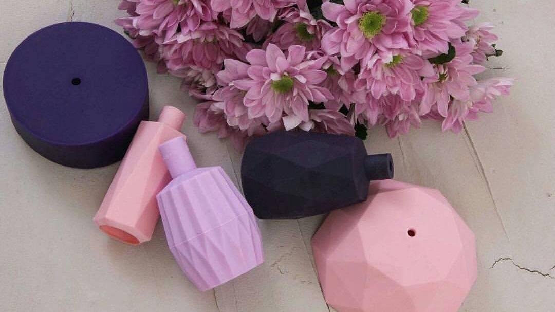 Farverige geometriske vaser i lilla og lyserød ved siden af lyserøde blomster.