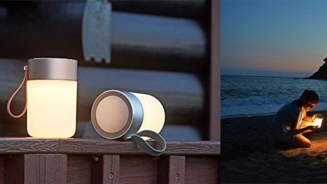 En moderne lommelygte står på en træoverflade, mens en person bruger den på stranden ved solnedgang.