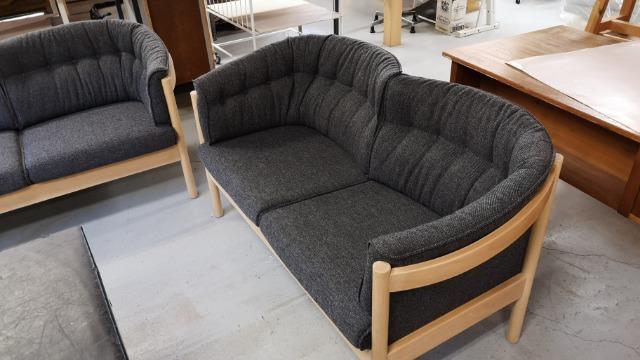 En moderne sofa med gråt stof og træramme, placeret i en møbelforretning.