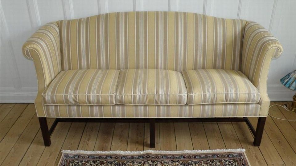 En stribet sofa med en lys beige farve og mørkt træben, placeret på et trægulv med et tæppe.