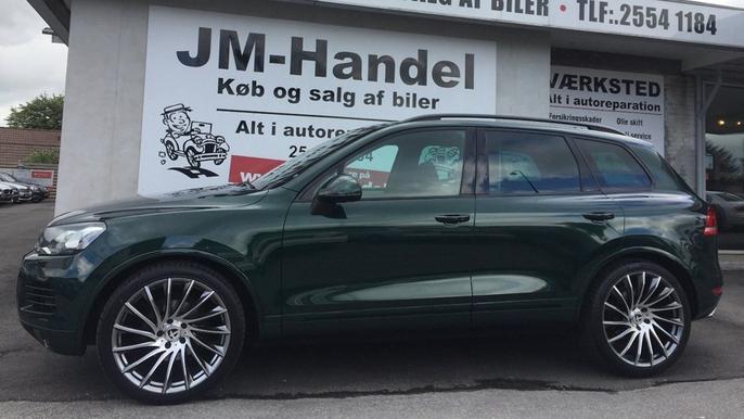 En grøn SUV parkeret foran en bilforhandler med store fælge og skiltet "JM-Handel".