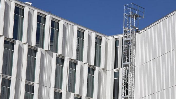 Moderne bygning med hvide facadepaneler og store vinduer under en klar blå himmel.