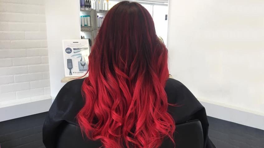 Langt, bølget hår i en rød og pink farve, set bagfra i en frisørsalon.