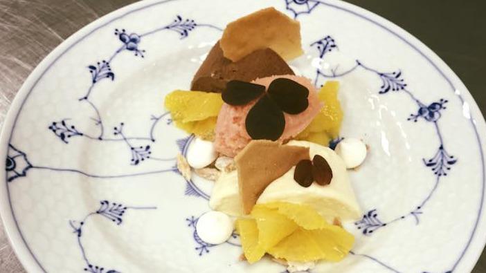 En tallerken med tre forskellige slags is, pyntet med appelsin, chokoladechips og små marcipanrunder.