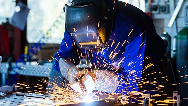 En svejser arbejder med en svejsemaskine, mens gnister sprøjter ud i et værksted.