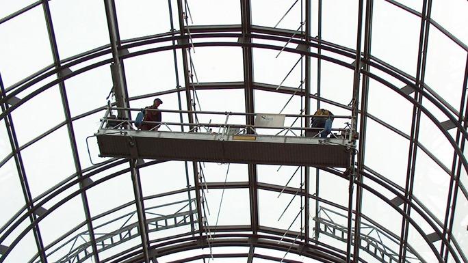 To arbejdere på en stillads under en glasstruktur, der arbejder på bygningens tag.
