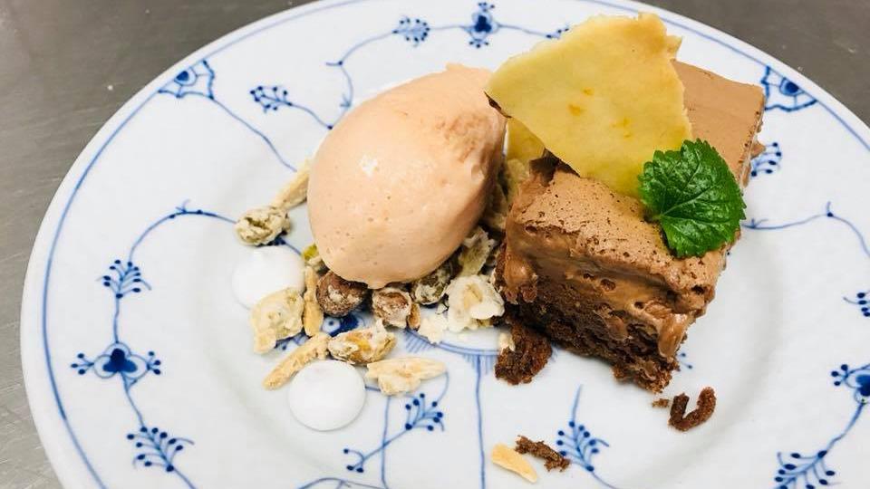 Lækker chokoladefondant med is, knas og pyntet med mynte på en dekorativ tallerken.