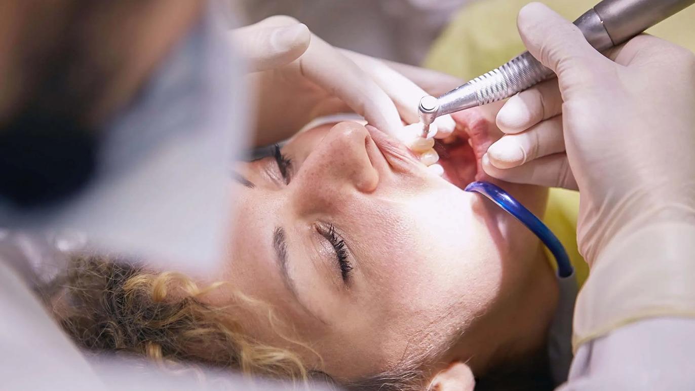 En tandlæge udfører en behandling på en patient, der ligger i tandlægestolen med åbne øjne.