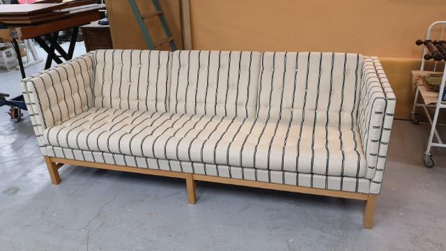 En stribet sofa med træben, placeret i et lyst rum med en neutral baggrund.